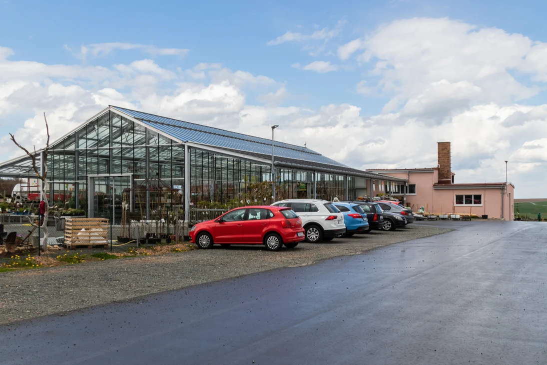Blick über den Parkplatz zum Verkaufsglashaus und dem dahinter liegenden Wirtschaftsgebäude