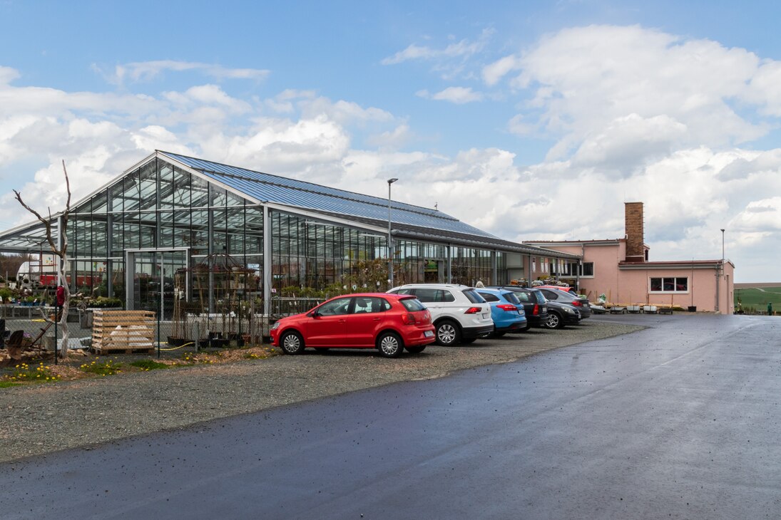 Blick über den Parkplatz zum Verkaufsglashaus und dem dahinter liegenden Wirtschaftsgebäude