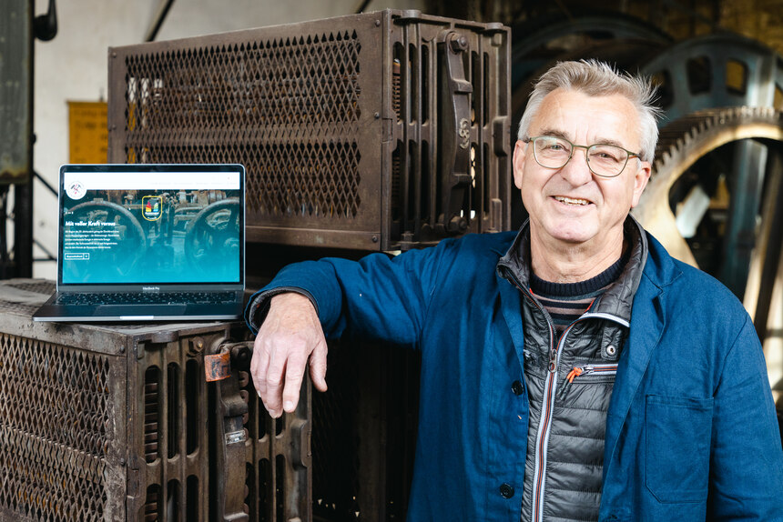 lächelnder Mann steht neben Laptop, auf dem die Webseite des Drei Brüder Schacht eV Freiberg zu sehen ist