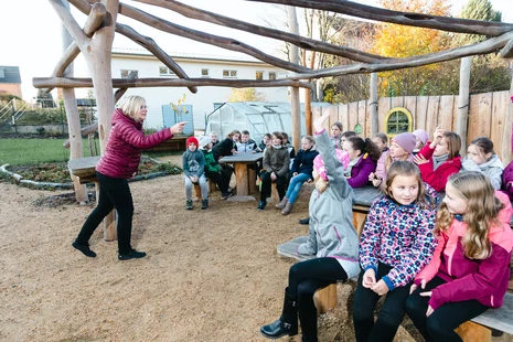 Eine stehende Lehrerin hält im Klassenzimmer draußen eine Unterrichtsstunde vor sitzenden Kindern