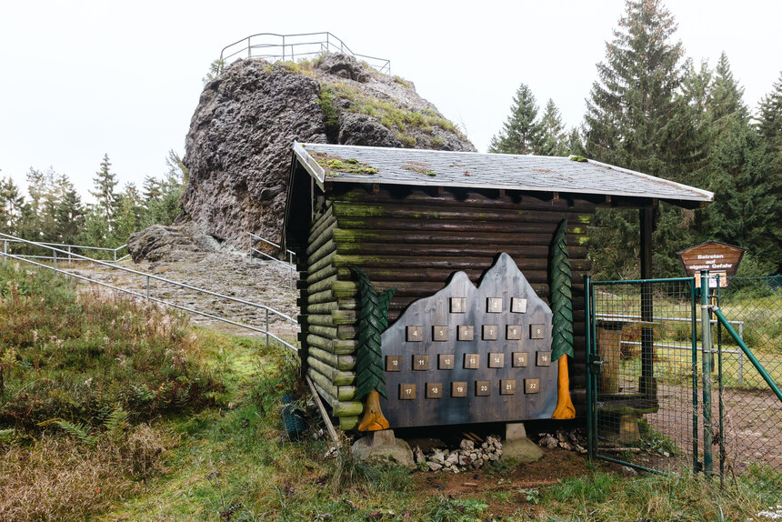 Vor dem Topasfelsen steht eine Holzhütte an deren Außenwand ein Spiel in Form einer Bergektte angebracht ist