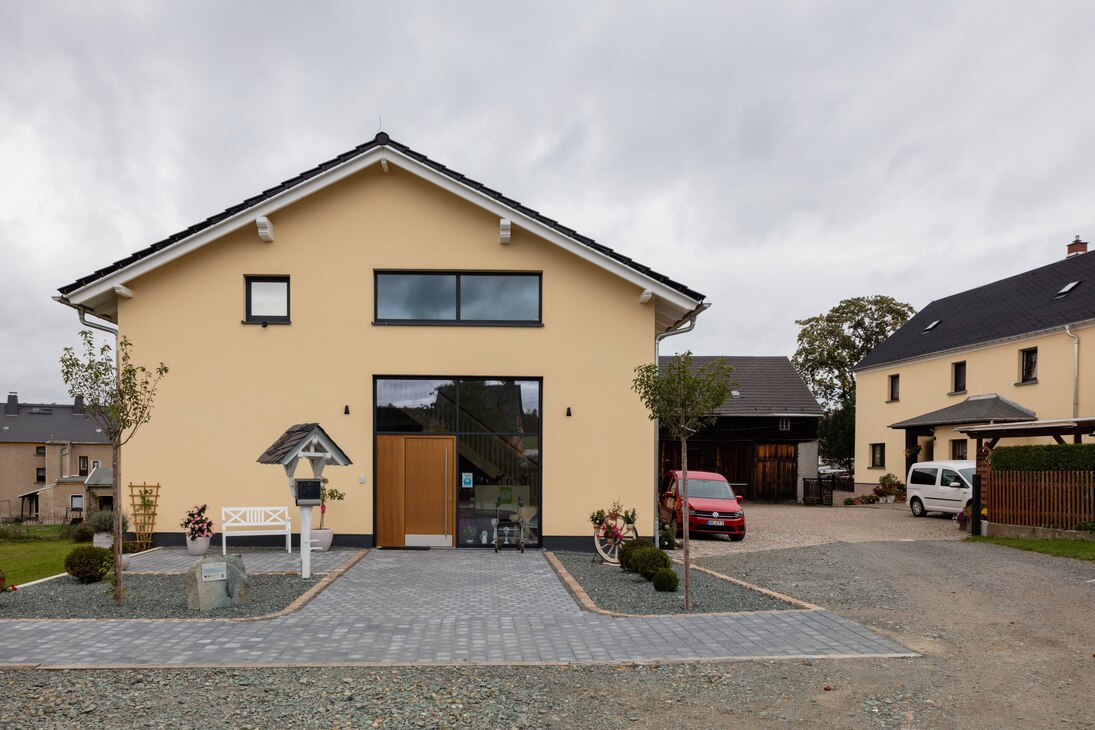 Die Außenansicht des Ersatzneubaus, fotografiert von der Giebelseite. Fassade in hellem Gelb gehalten mit großer Glasfront.