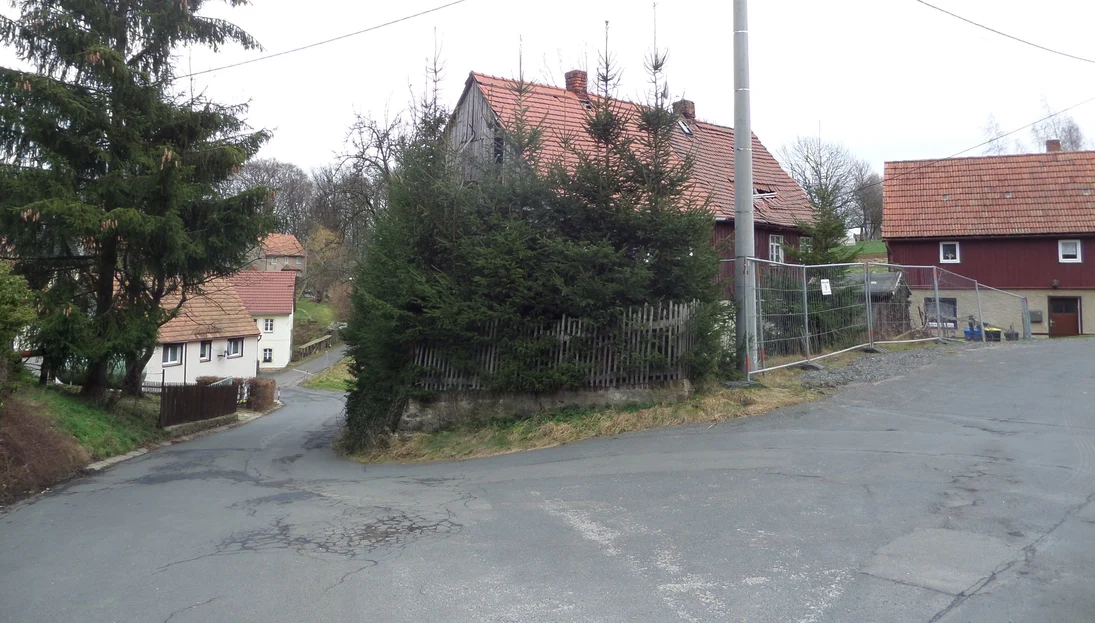 geteerter rissiger Straßenbelag, zwei Gebäude im ansteigenden Gelände