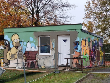 Blick auf die Hütte. Die Fassade ist mit Graffiti gestaltet.