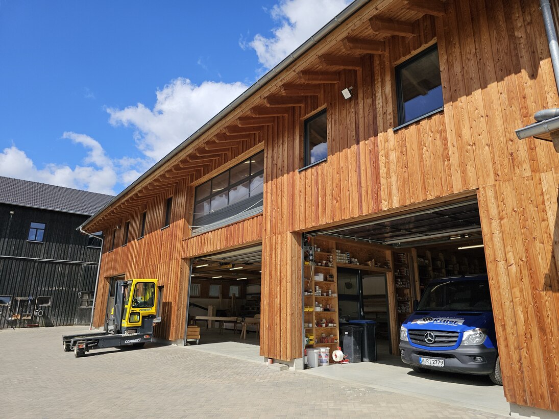 Blick auf die Halle mit geöffneten Toren und auf den gepflasterten Vorplatz mit Gabelstapler und Firmenfahrzeug
