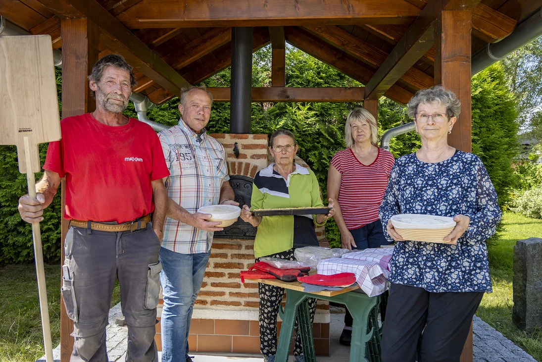 fünf Menschen stehen vor einem überdachten Holzbackofen, sie halten Brotschieber, Backblech und Kuchenformen in den Händen
