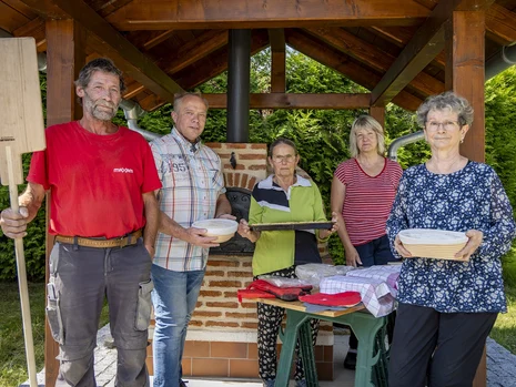 fünf Menschen stehen vor einem überdachten Holzbackofen, sie halten Brotschieber, Backblech und Kuchenformen in den Händen