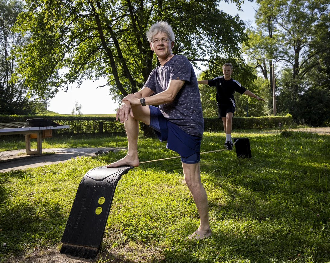 ein Mann steht barfuß auf einer Wiese und ein Junge balanciert daneben auf einer Slackline