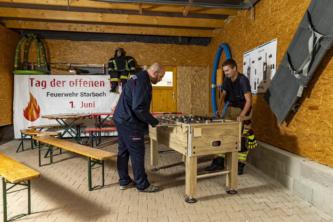 zwei Feuerwehrmänner spielen an einem Tischkicker