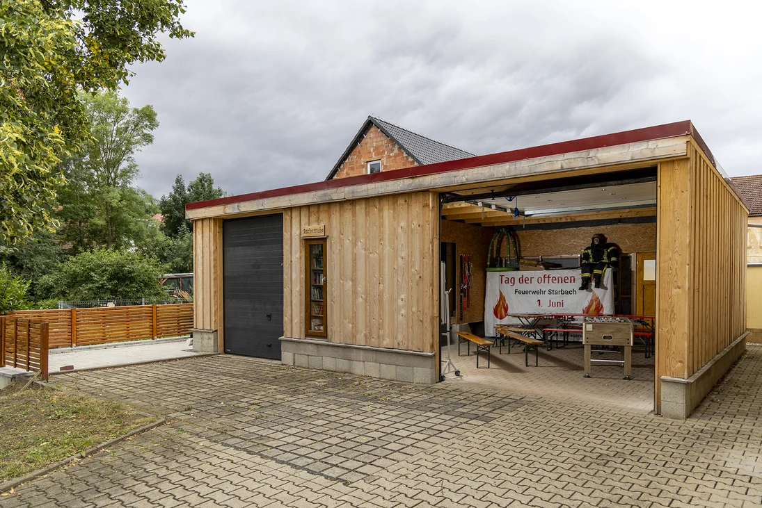 eine offene Holzgarage auf einem gepflasterten Platz