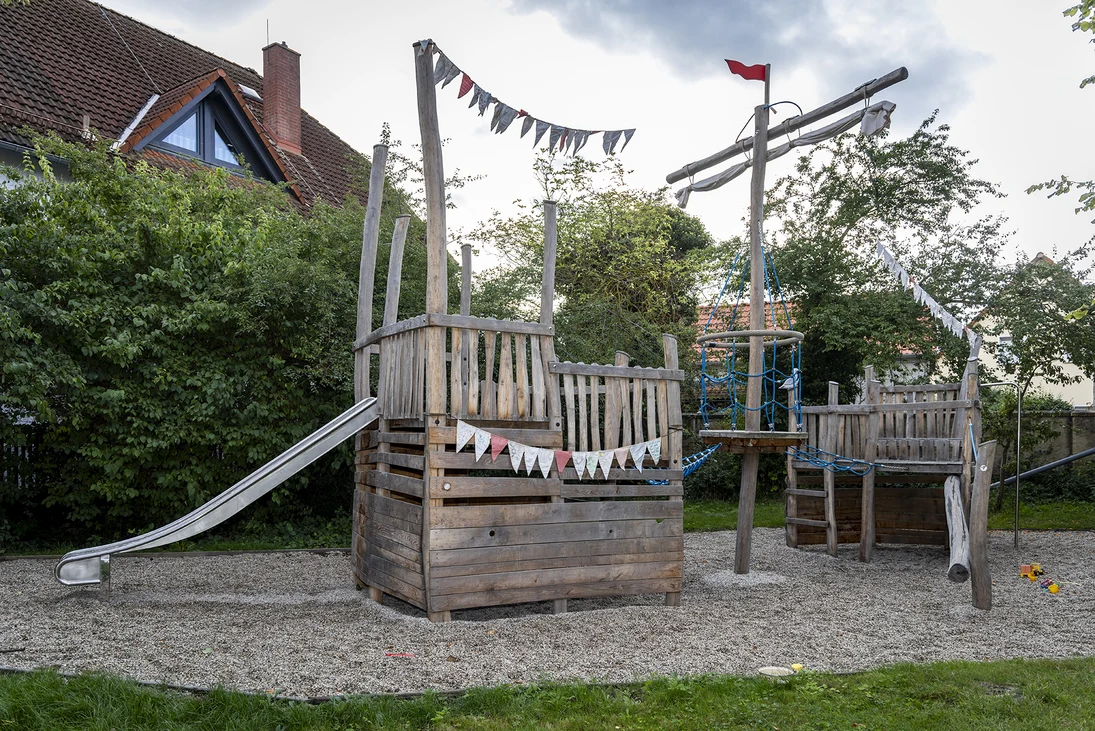 ein großes hölzernes Spielschiff mit einer metallenen Rutsche und Wimpelketten