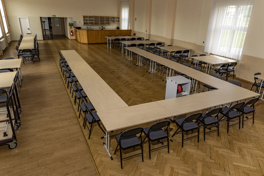 Blick in einen großen Saal mit Parkettboden und einem u-förmigen Tisch mit vielen Stühlen