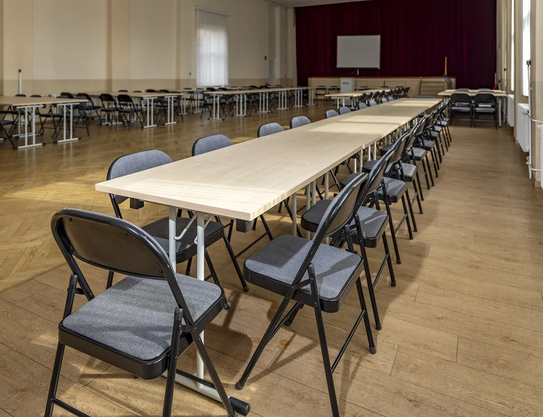 Blick in einen großen Saal mit Parkettboden und einem langen Tisch mit vielen Stühlen