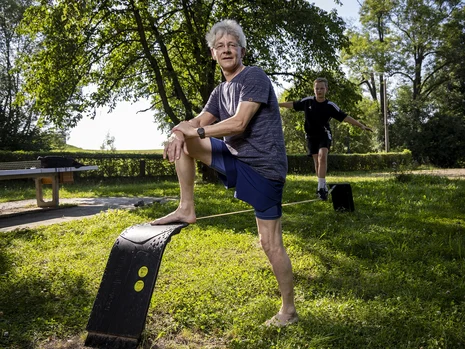 ein Mann steht barfuß auf einer Wiese und ein Junge balanciert daneben auf einer Slackline