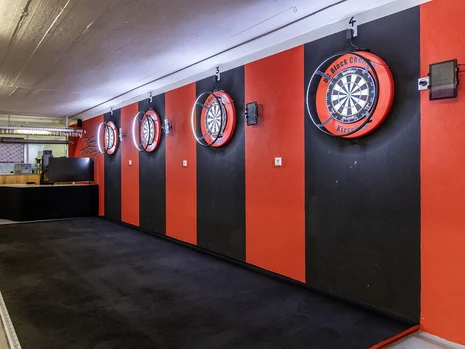 Blick auf eine schwarz und rot gestrichene Wand, an der vier Dartscheiben hängen