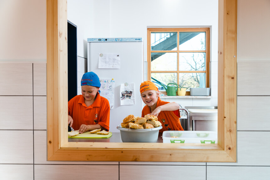  Zwei Kinder sind durch ein Ausgabefester in der Küche zu sehen. Sie bereiten belegte Brote zu