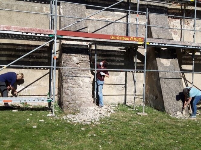 Drei Personen schlagen Putz von der Giebelwand des Pfarrhauses ab