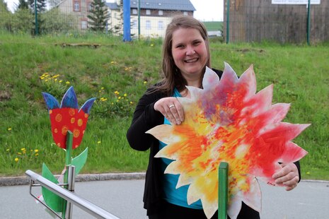 Eine junge Frau hält eine große, bunt bemalte Holzblume in der Hand