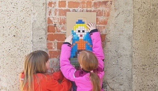 zwei Mädchen bringen ihr buntes Bild an einer Hausfassade an