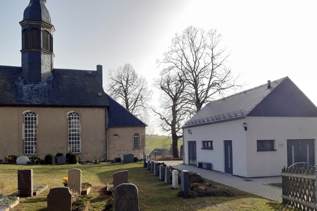 Die Kirche steht rechtwinklig zur Trauerhalle, beide umschließen den Friedhof.