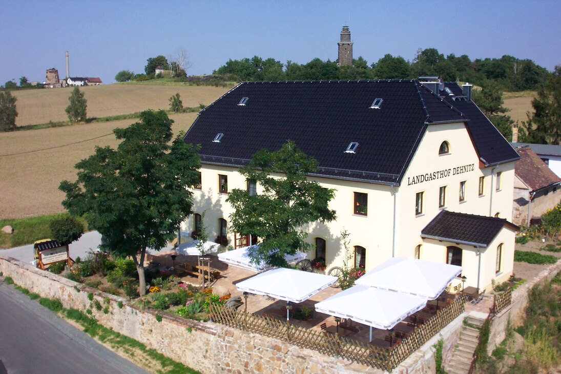 Der Landgasthof mit Freisitz inmitten von Feldern, im Hintergrund ein Berg mit Bismarckturm.