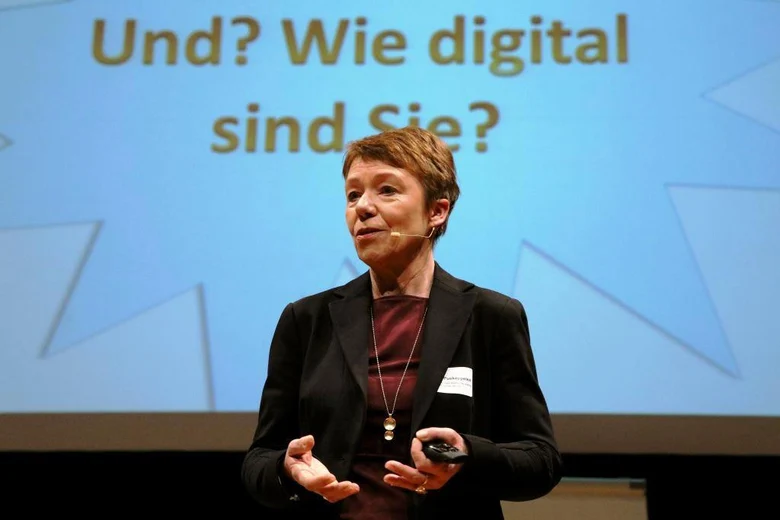 Frau Marika Puskeppeleit in der Mitte des Bilde beim Vortrag »#Land2037 - Ein Blick in die digitale Zukunft der ländlichen Räume«. Hinter ihr auf der Leinwand ein bläulicher Stern mit dem Schriftzug »Und? Wie digital sind Sie?«.