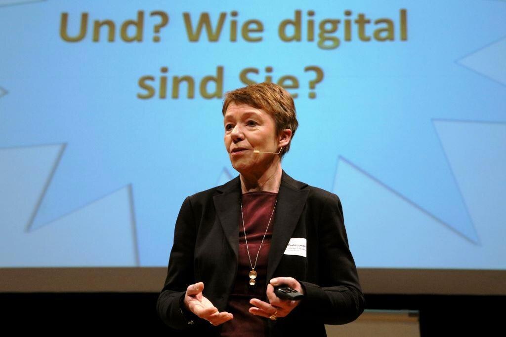 Frau Marika Puskeppeleit in der Mitte des Bilde beim Vortrag »#Land2037 - Ein Blick in die digitale Zukunft der ländlichen Räume«. Hinter ihr auf der Leinwand ein bläulicher Stern mit dem Schriftzug »Und? Wie digital sind Sie?«.