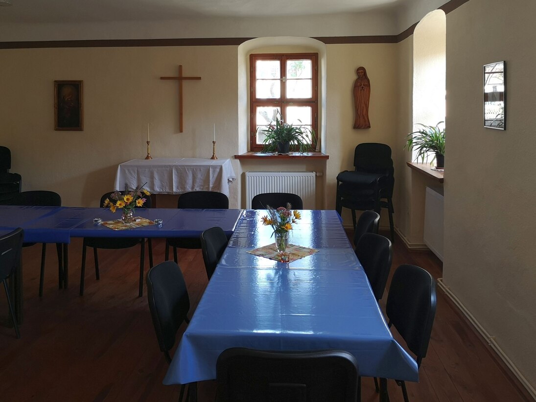 Ein langgestreckter Tisch in einem Raum mit Kreuz und Heiligenfigur an der Wand