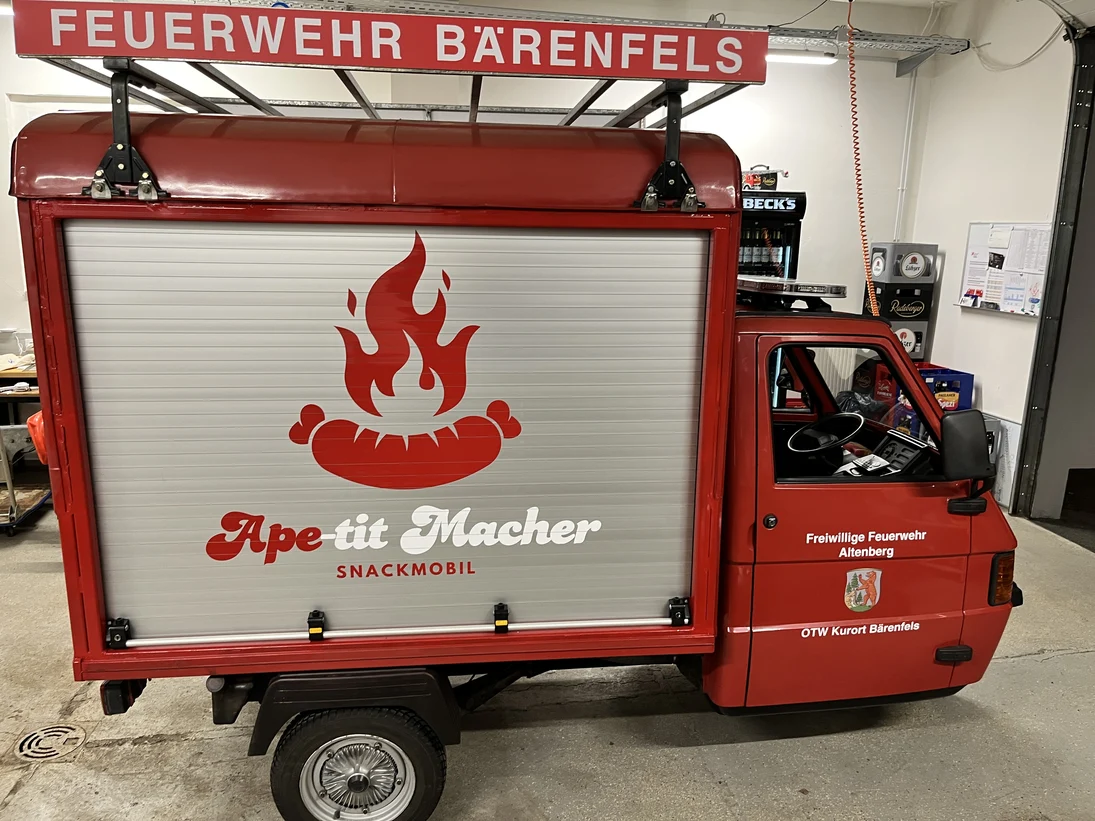 rotes italienisches Dreirad-Nutzfahrzeug Piaggo APE als Feuerwehr-Einsatzfahrzeug mit der Aufschrift "Ape-tit Macher"