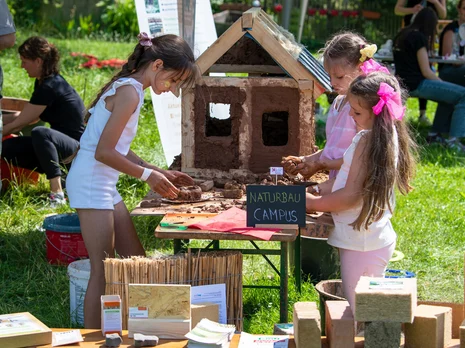 Drei Mädchen vom Naturbaucampus stehen an ihrem Tisch und basteln. Der Tisch steht auf einer Wiiese.