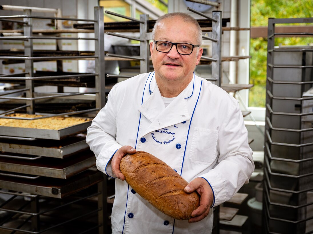 Der Bäckermeister steht mit einem Brot in den Händen in der Backstube.