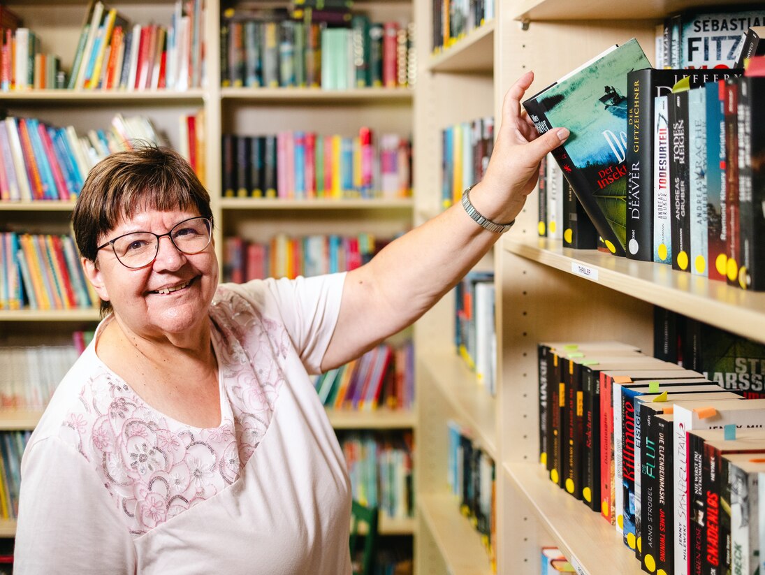Eine Frau zieht ein Buch aus einem Regal der Bücherei.