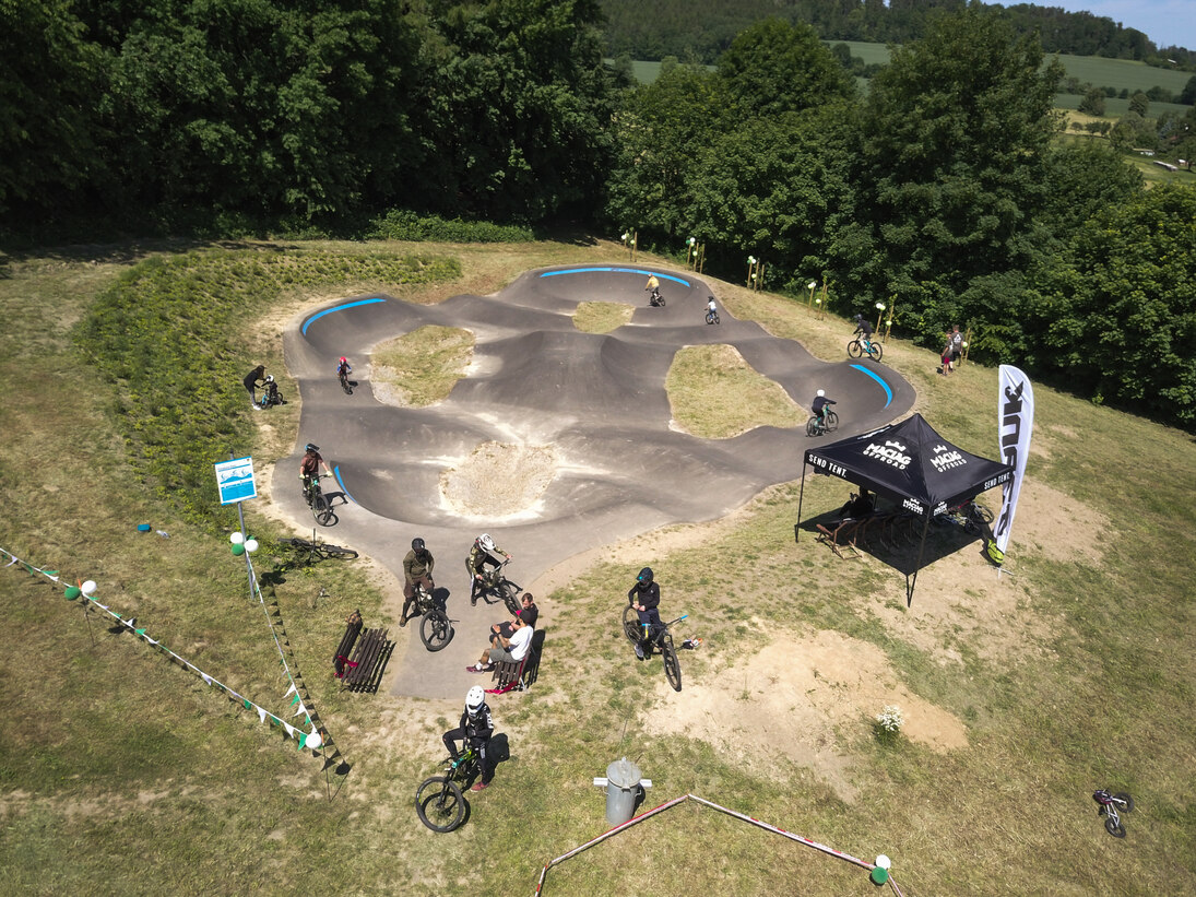 Luftaufnahme der neuen Pump Track Anlage mit zahlreichen Mountainbiker auf und an dem Parcours