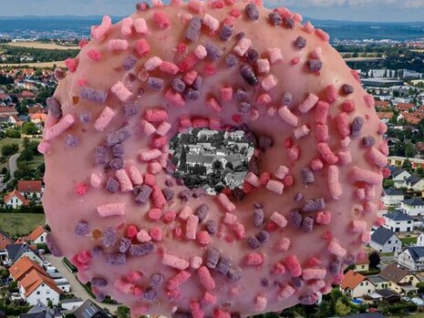 Ein Riesendonat mit rosa Zuckerglasur und Streuseln schwebt über einem Dorf