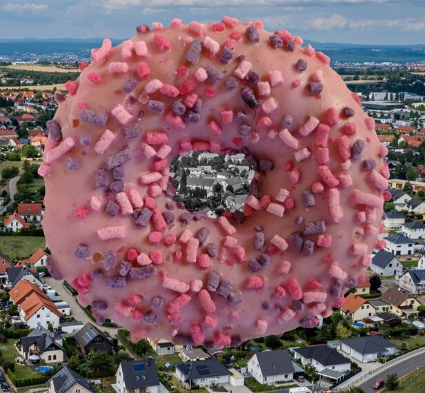 Riesendonut mit rosa Zuckerguss schwebt über einem Dorf