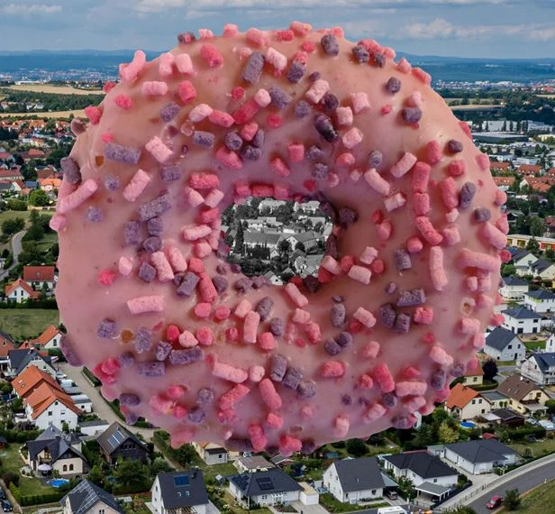 Riesendonut mit rosa Zuckerguss schwebt über einem Dorf