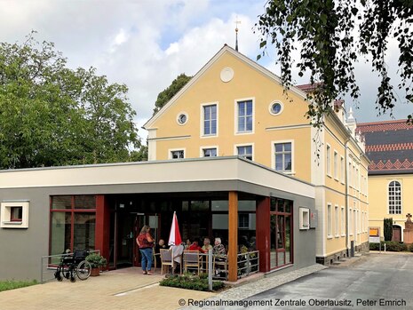 Gebäudeensemble mit Pfarramt und Kirchenschiff im Hintergrund, im Vordergrund der moderne Anbau an der alten Kirchschule