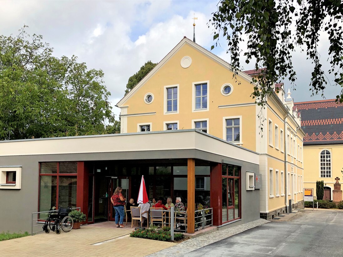 Gebäudeensemble mit Pfarramt und Kirchenschiff im Hintergrund, im Vordergrund der moderne Anbau an der alten Kirchschule