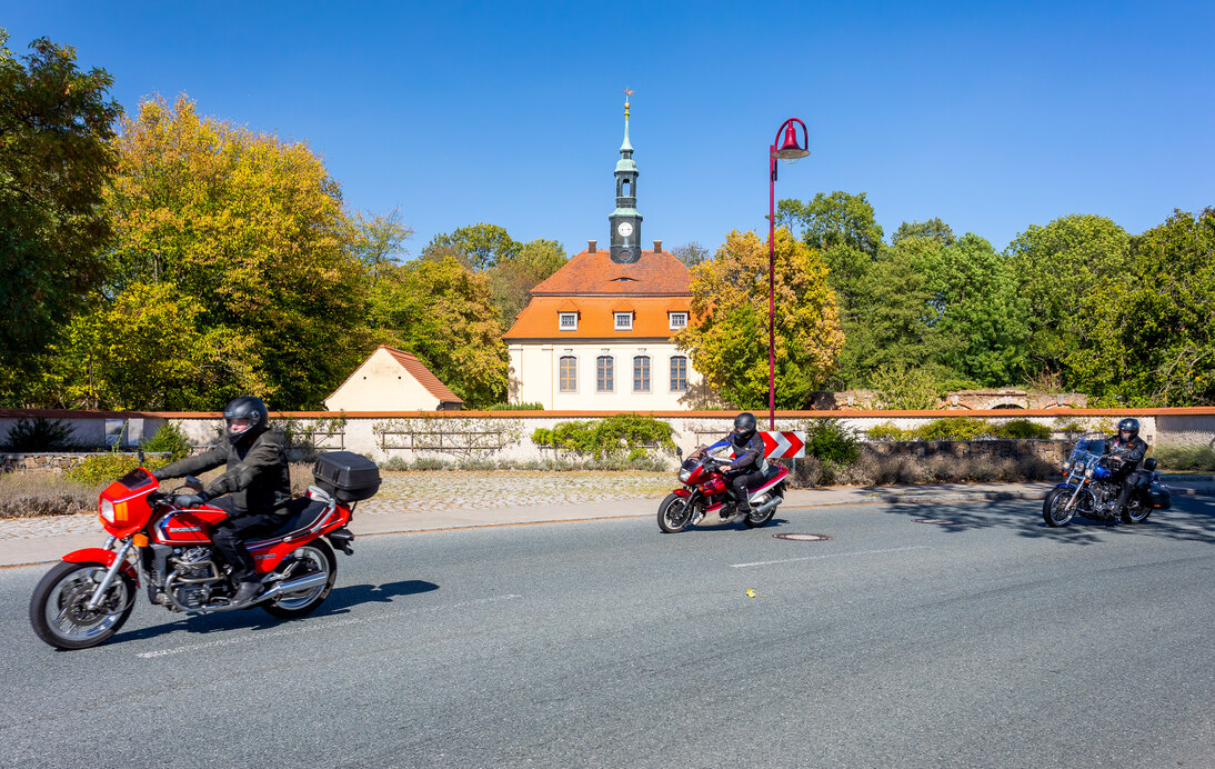 Biker fahren auf der Straße vorbei an der Schlosskapelle in Tiefenau.