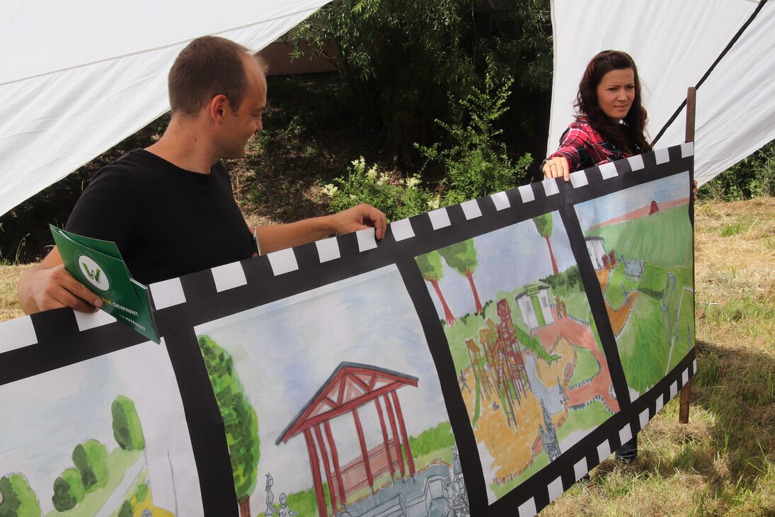 Ein Frau und ein Mann halten ein Plakat hoch, auf dem die Entwürfe des Mehrgenerationenspielplatzes in Waldkirchen zu sehen sind.