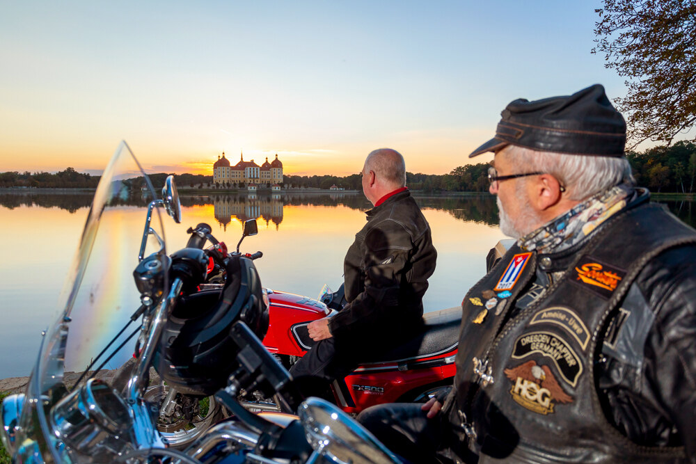 Zwei Biker auf ihren Motorrädern vor dem Moritzburger Teich, im Hintergrund ist das Wasserschloss Moritzburg zu sehen.