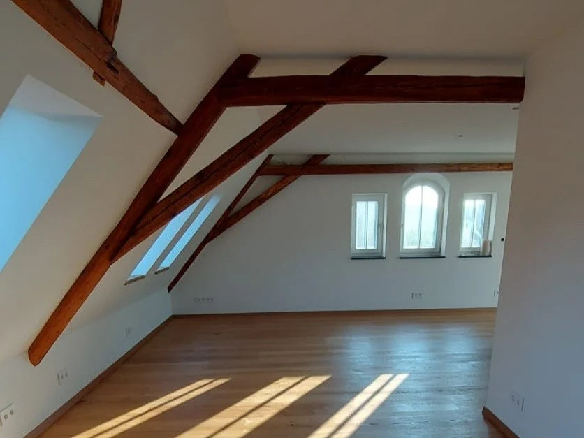 Innenansicht mit Dachschräge und sichtbaren Balken sowie drei Fenstern