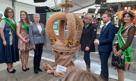 Ministerpräsident Michael Kretschmer und Dr. Monika Michael, Präsidentin des Sächsischen Landfrauenverbandes, stehen bei der Übergabe der schönsten Erntekrone 2022 mit den Erntehoheiten um die Siegerkrone