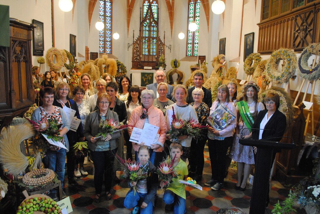 Gruppe von Menschen mit Blumen und Präsenten steht im Altarraum der Kirche, im Hintergrund sind Erntekronen- und kränze zu sehen