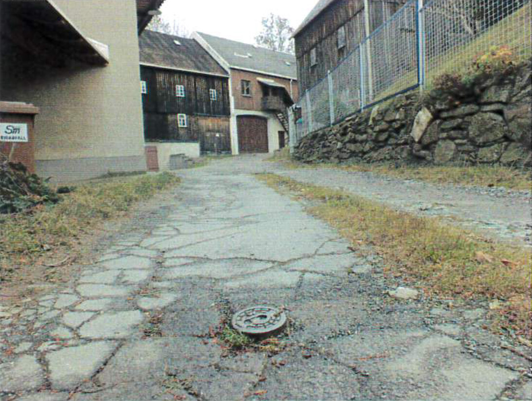 Straße vor der Baumaßnahme mit altem Straßenbelag und alter Mauer