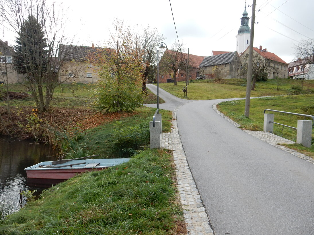 Kirchweg, Abschnitt am Dorfteich, die neue Fahrbahn ist abgegrenzt mit Muldenrinnen, im Hintergrund die Kirche