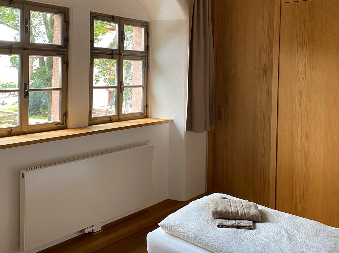 Ferienwohnung mit Holzbalkendecke und einem Gästebett auf dem Handtücher bereit liegen.