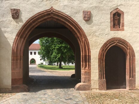 Ein kleiner und ein großer Torbogen mit Blick in den Innenhof des Klosters mit einem markanten Baum.