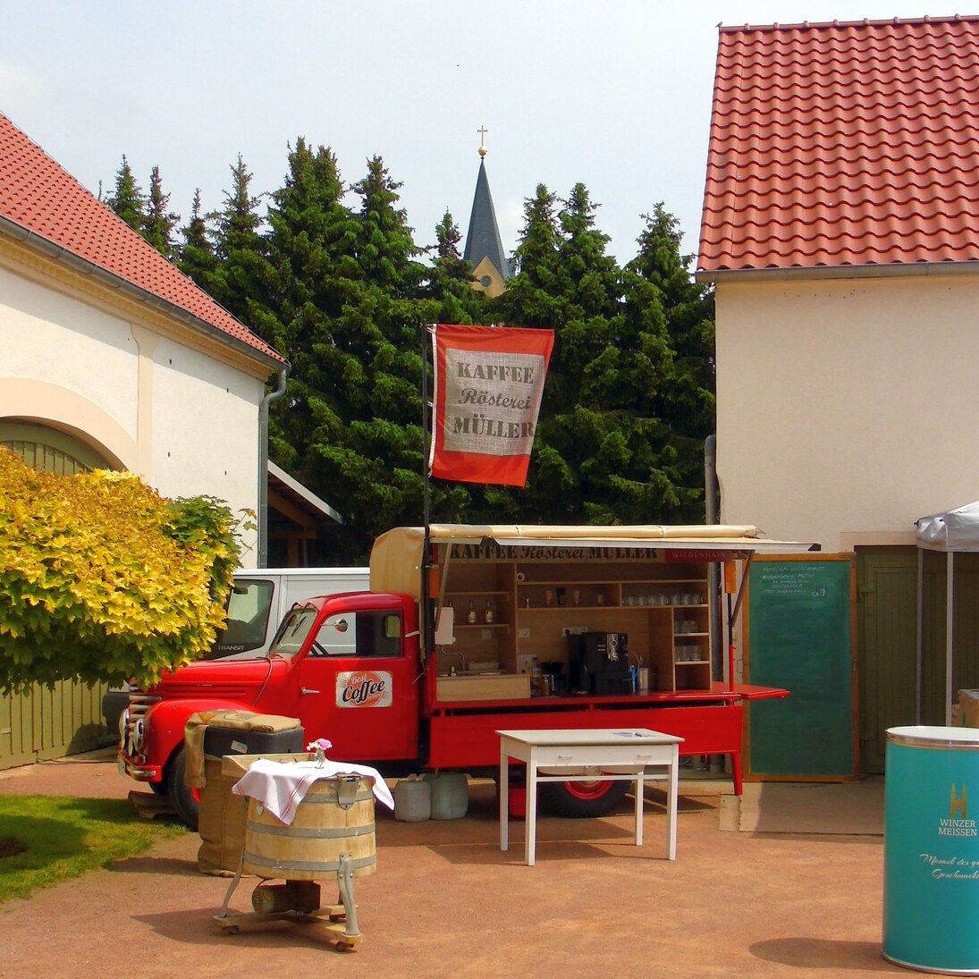 Das Kaffeemobil, aufgestellt zum Tag der offenen Rösterei. Bänke und Tische im Vordergrund laden Besucher zur Kaffeeverkostung am Kaffeemobil ein.