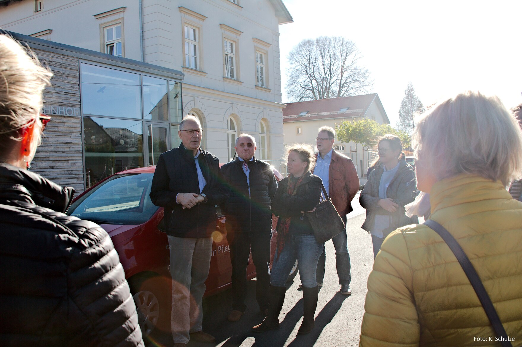 Wolfgang Ahnert hält Ansprache zu den Exkursionsteilnehmern vor dem Generationenbahnhof Erlau. Im Hintergrund links moderner Anbau, in der Mitte der sanierte Altbau des Bahnhofs Erlau.